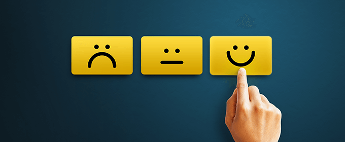 Drei auf gelbe Karten gemalte Smileys, die verschiedene Emotionen darstellen, wobei ein Finger auf die Karte mit dem glücklichen Smiley zeigt.