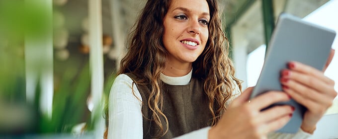 E-Commerce: Eine Frau sitzt an einem Tisch und schaut auf ihr Tablet.